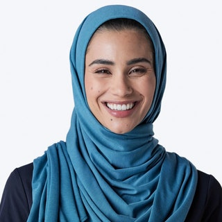 Medelita Medical Hijab model looking into the camera and smiling wearing a blue hijab on white background